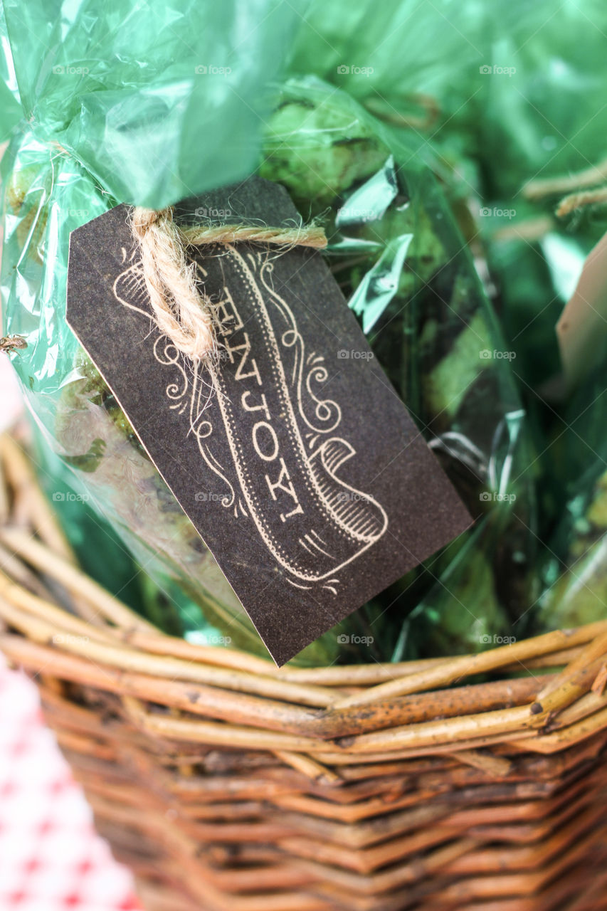 Chalkboard tag reading "enjoy" attached to green party favors with twine in a wicker basket