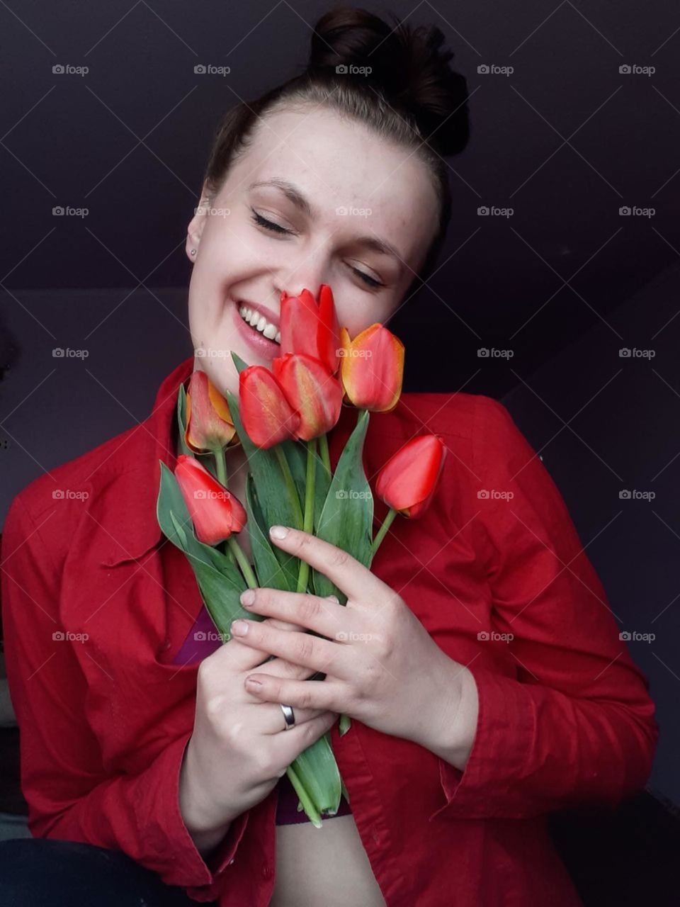 A light-skinned girl holds a bouquet of bright red tulips near her face and smiles.