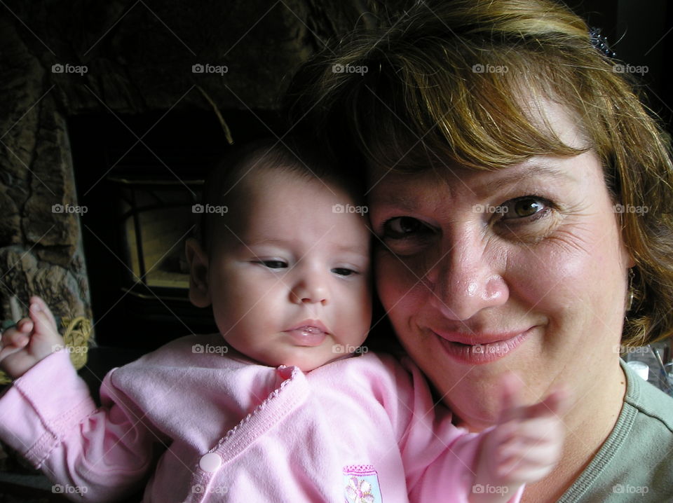 A closeup of mom and her baby. Mom is smiling with love and affection & is holding the baby close to her face. The baby just woke up from a nap and is exploring her surroundings from the safety of her momma’s arms. 