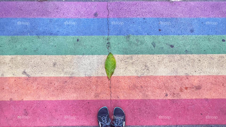 Standing in front of the rainbow colours on the ground with a leaf and a crack in the middle of it.