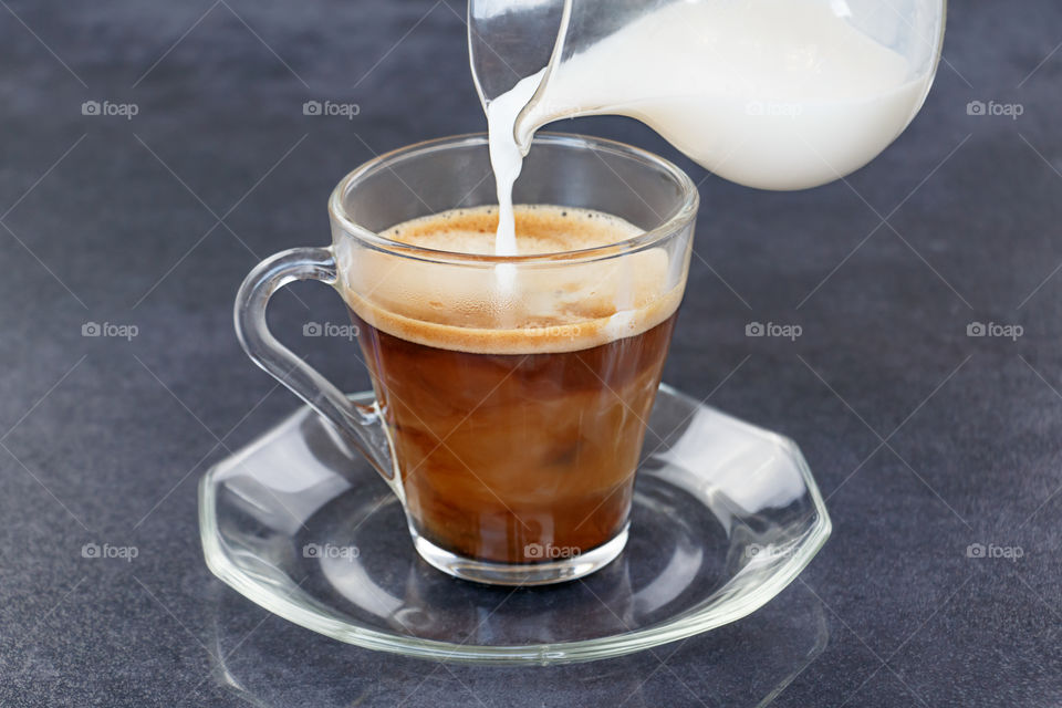 Pouring milk from a jug into a cup of black coffee