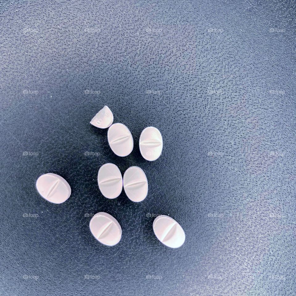 Several pills are scattered on a black background. The pills are white and oval shaped. 