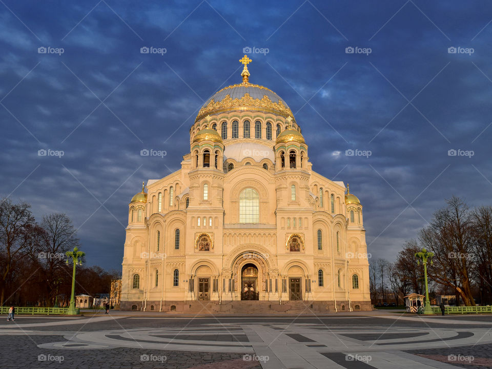 Beautiful light church in the rays of the setting sun on the background of the dark blue cloudy sky