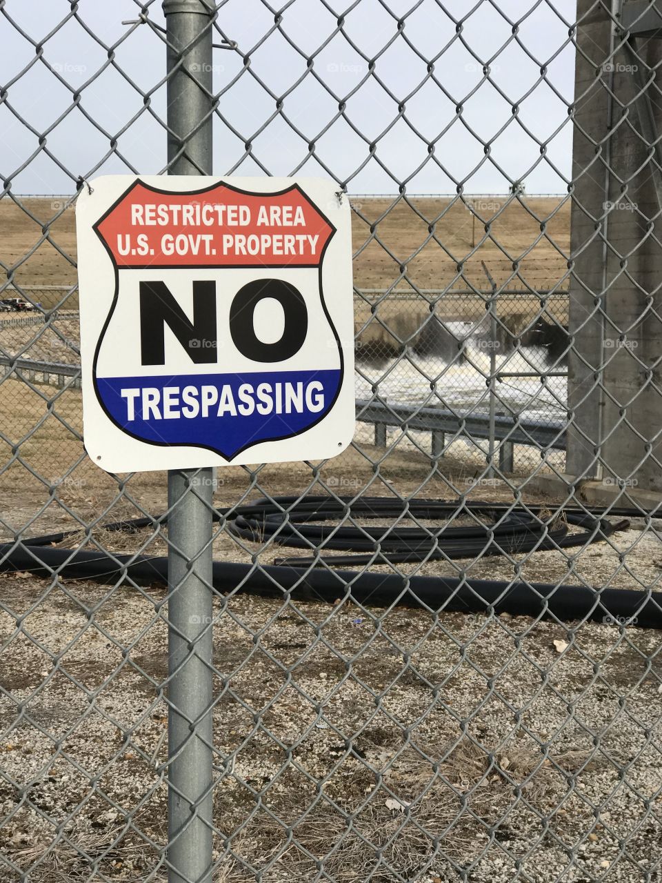 US Army Corps of Engineers, restricted area, US Govt Property, no trespassing sign, winter January, In background Dam and water release area beyond chain link fencing at Oologah Lake Oklahoma.