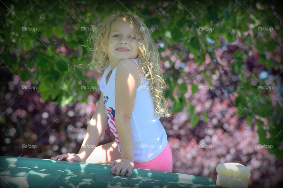 Beautiful little girl with blonde curls, sitting pretty on the roof of her playhouse. 