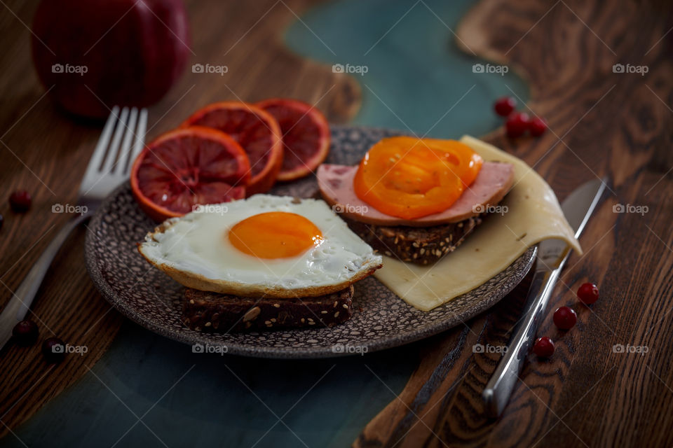 Grain bread with egg, tomato, cheese and bacon on ceramic plate with red orange to desert