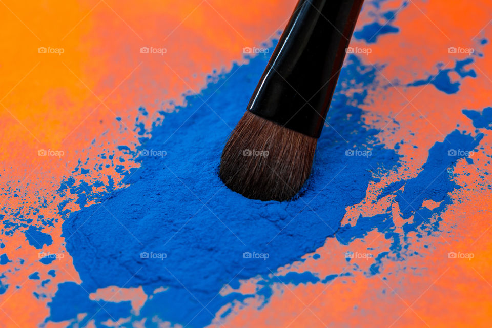 orange and blue - image of make-up brush on blue powder with orange background close-up