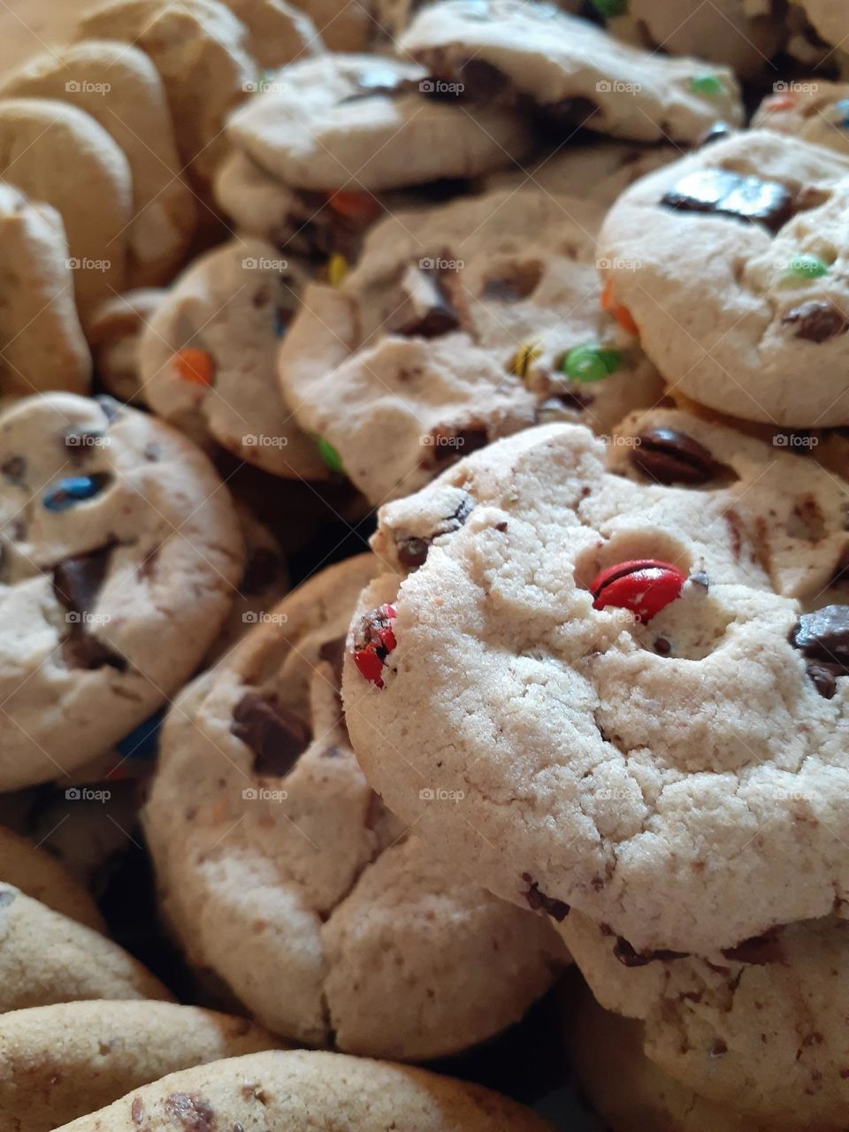 A bunch of delicious chocolate chip cookies with different colored candy coated chocolate in them. Great for dessert.