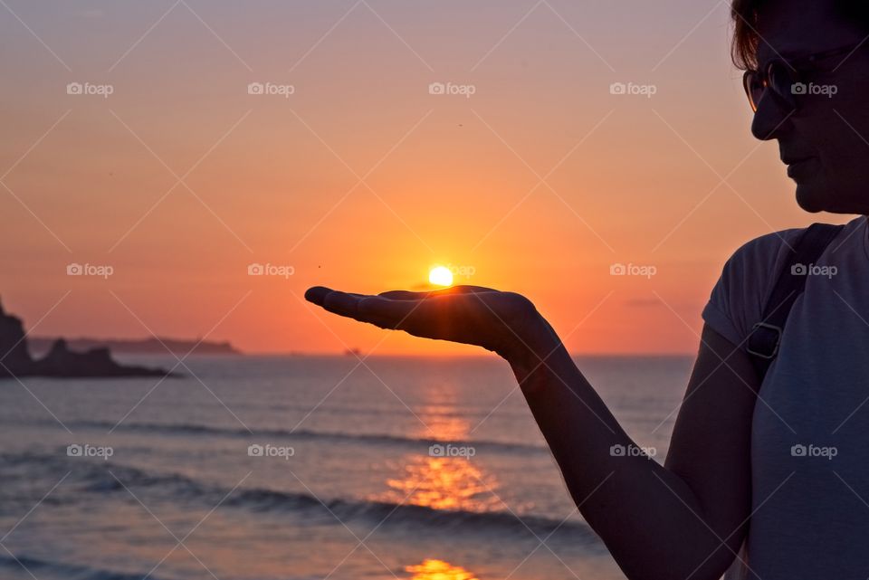 A woman holds the sun on her hand at sunset