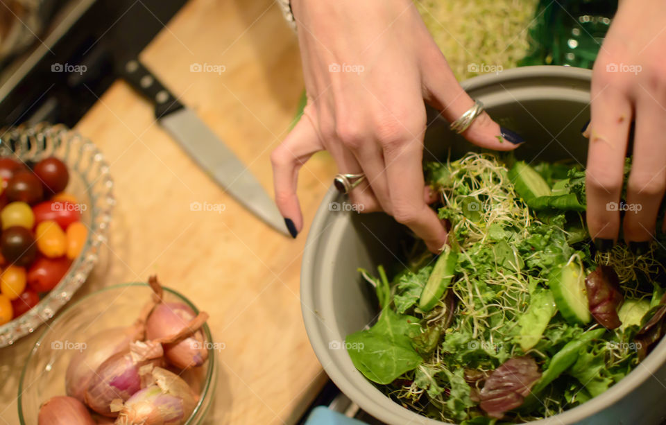 Woman Making healthy salad at home with organic ingredients and healthy vegetables, mixed greens, sprouts and shallot 