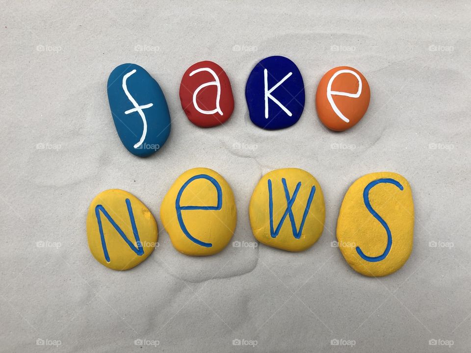 Fake news text composed over white sand with colored stones