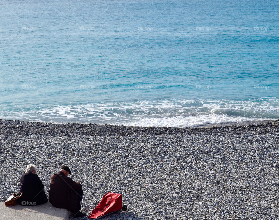 Elderly couple sitting by the pebble beach in Nice, France.