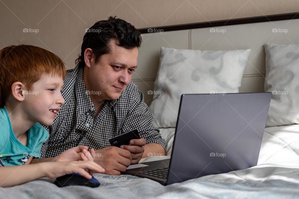 Father and son have fun together, at home they buy toys online shopping sit by the bed with a laptop, close-up portrait life style