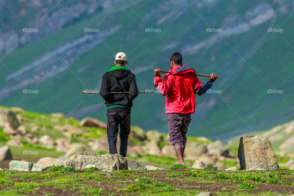 two people or shepherds walking with sticks on their shoulder and talking briefly