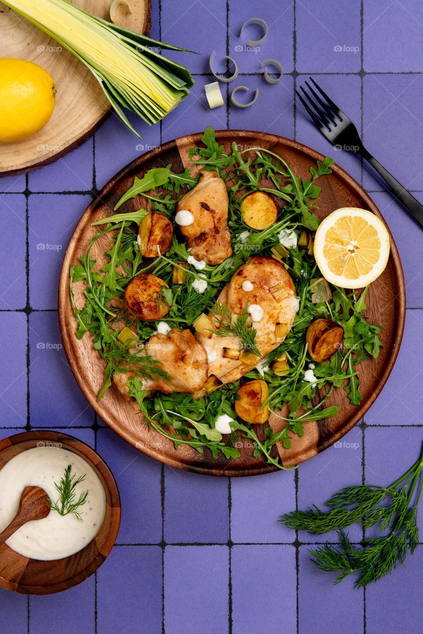Colorful flat lay of a roast chicken and arugula dish on a purple surface 
