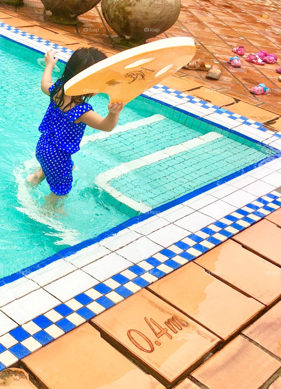 Pool time; little girl making way to side of kid’s pool with a surf board float 