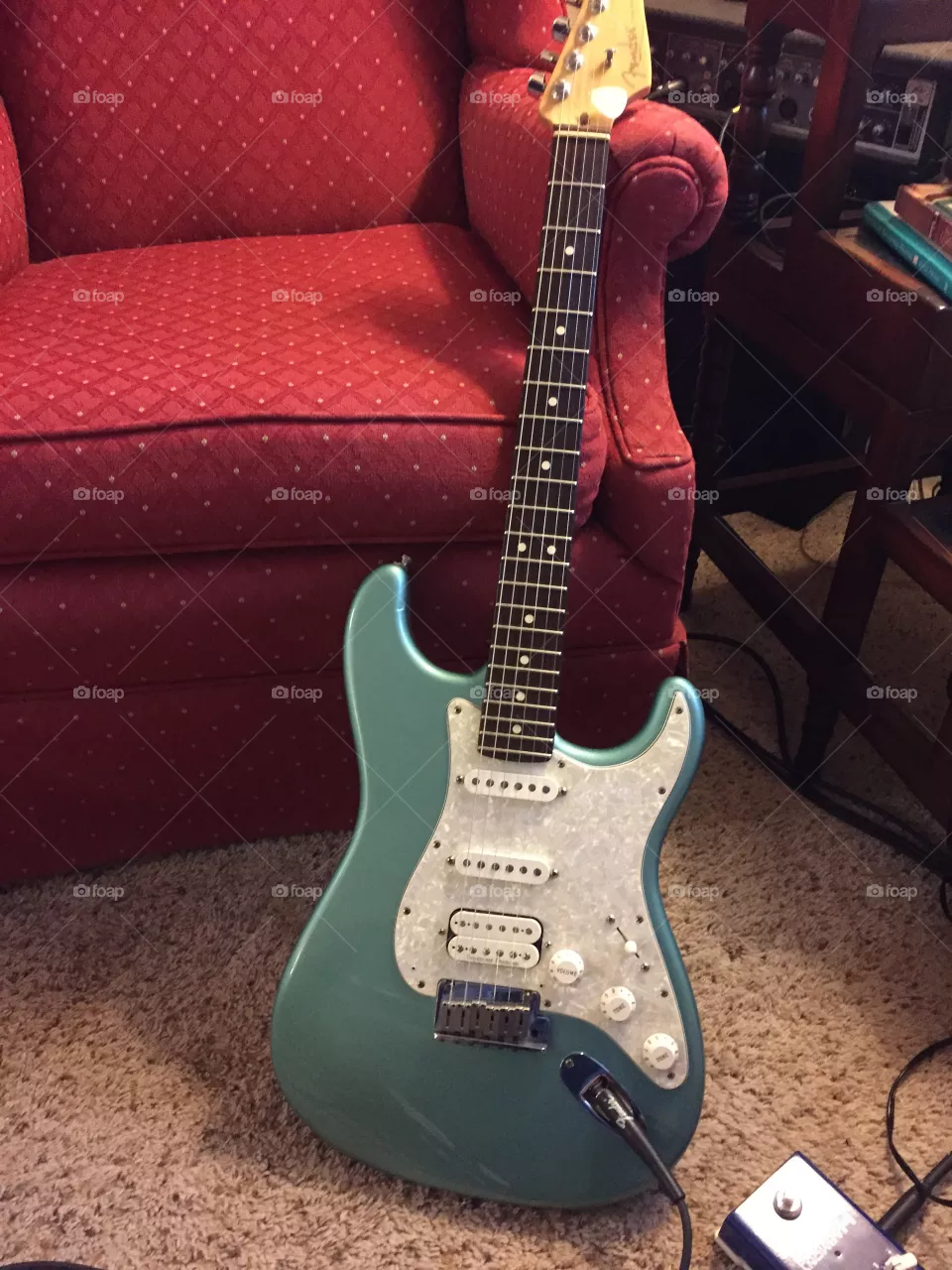 A blue electric  stratocaster guitar leaning against the chair tuned up plugged in and waiting to be played.