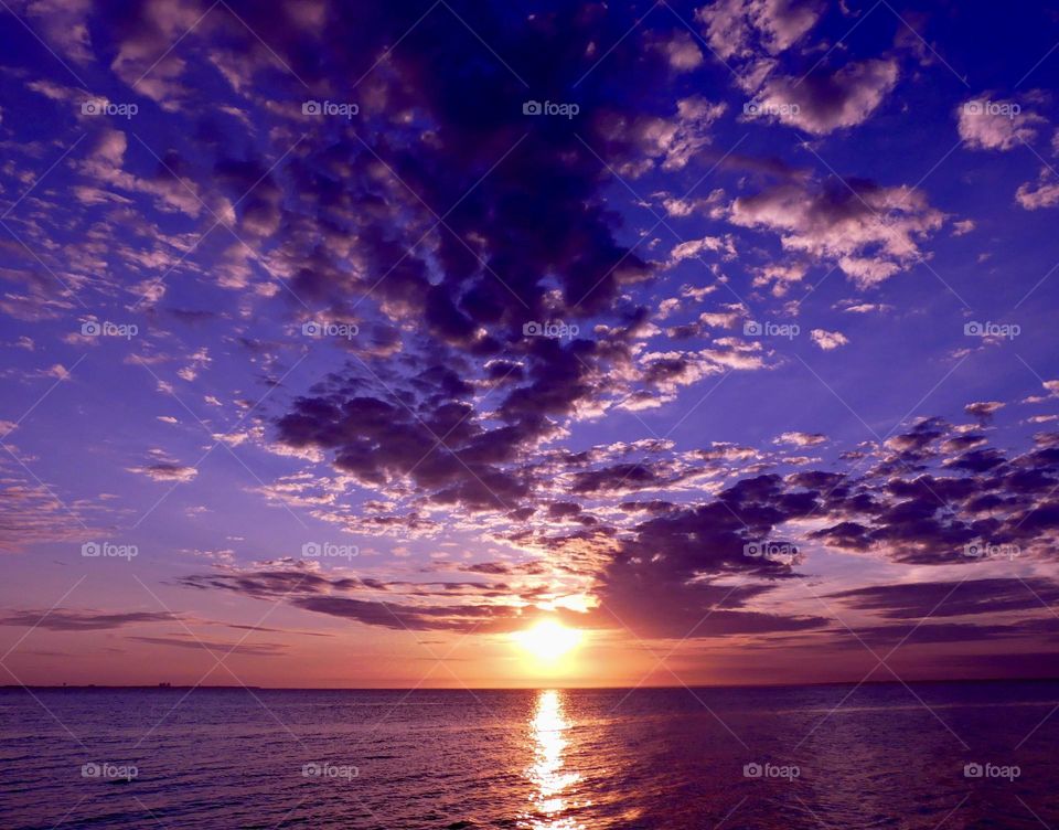 Mesmerizing sunset over the ocean with mauve colored sky and floating puffy clouds over an open waterway. The effects of weather on our moods, colors and emotions depends on our behavior and on how we think