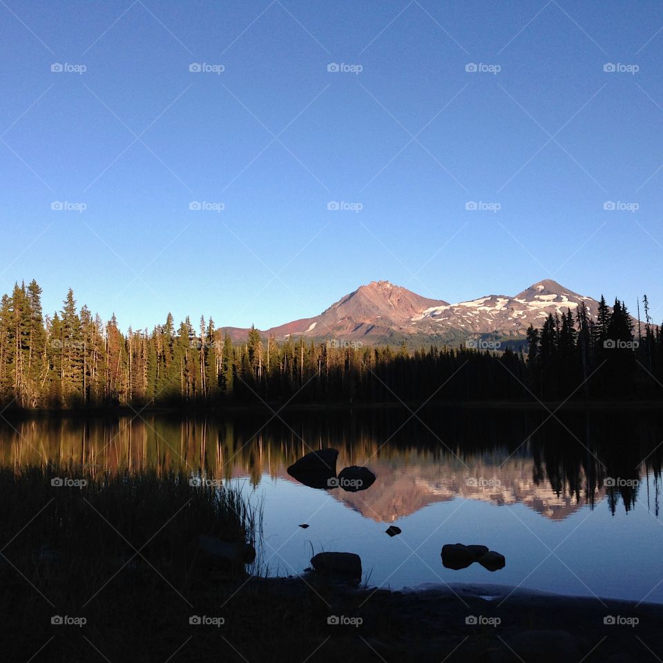 Two of the Three Sisters in Oregon’s Cascade Mountain Range reflecting in the calm waters of Scott Lake in the Deschutes National Forest as the evening light fades away on a beautiful fall evening. 