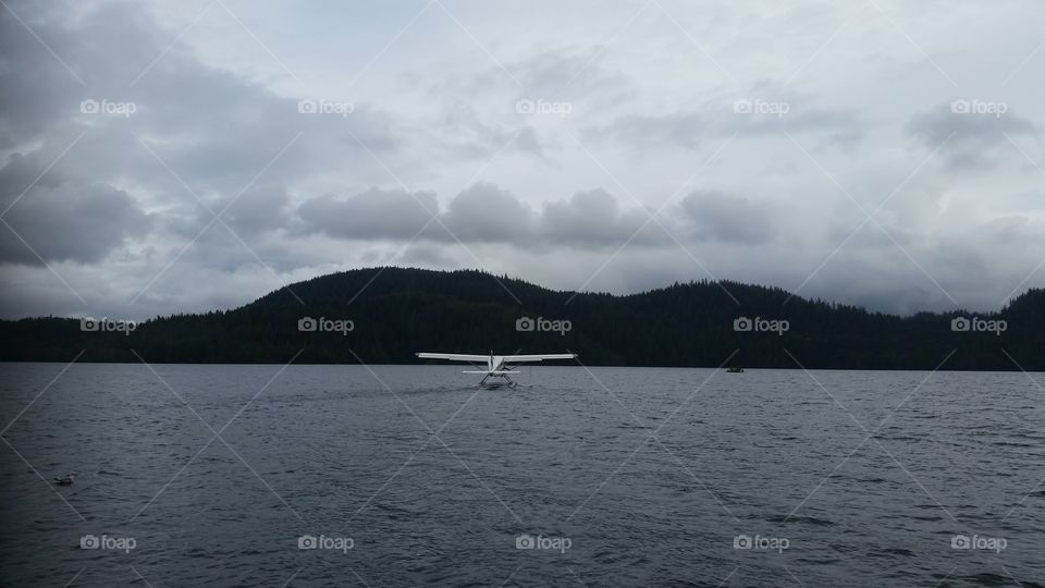 Bush sea plane landing on Ocean water on cloudy day with land in view in Skagway Alaska