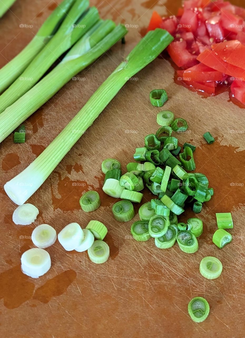 fresh green onion chopped up finely on a wooden cutting board with cut up tomatoes