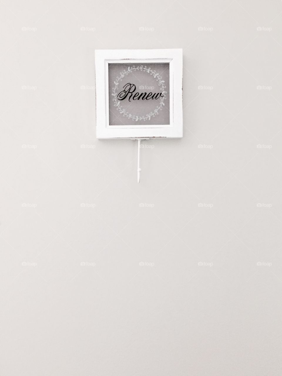 "Renew" - glass and wood plaque with hook and  the word "Renew" painted in black cursive lettering with a white laurel wreath around it on a neutral-colored wall