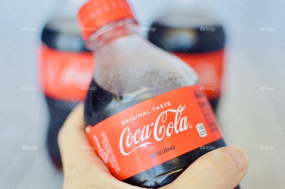A hand holding a bottle of Coca-Cola on a white rustic background