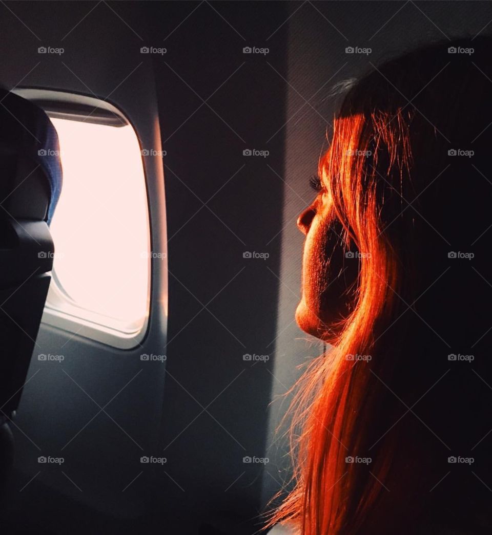 A blonde looking with hope from the window seat in an airplane during sunset 