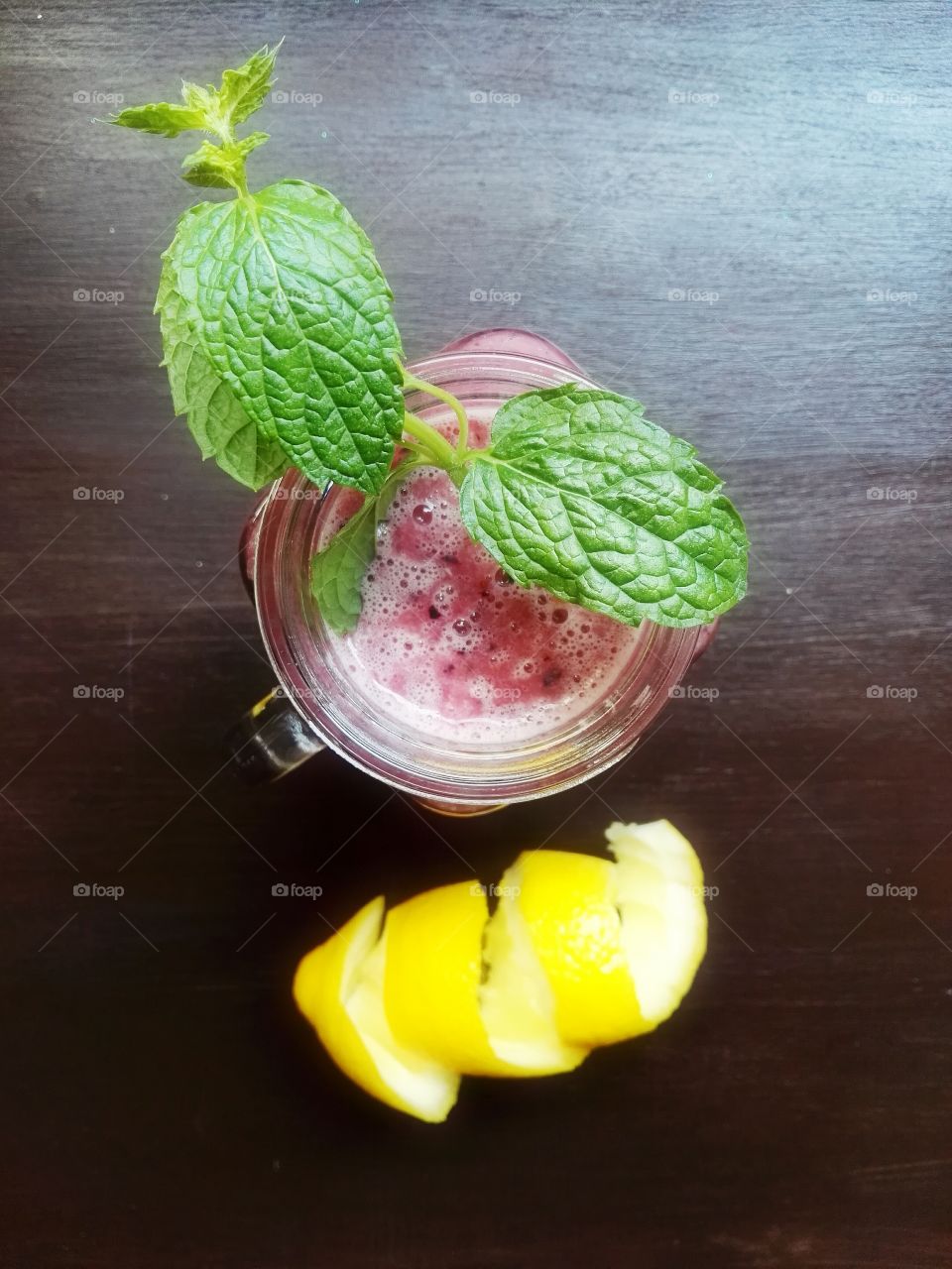 Red fruit smoothie with mint leaves on dark background, top view