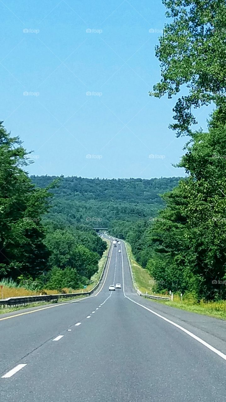 Road trip driving on long two lane highway through green mountains, destination towards Blue Grass State of Kentucky. Sky is blue, with clear road ahead of us, we can see for miles!