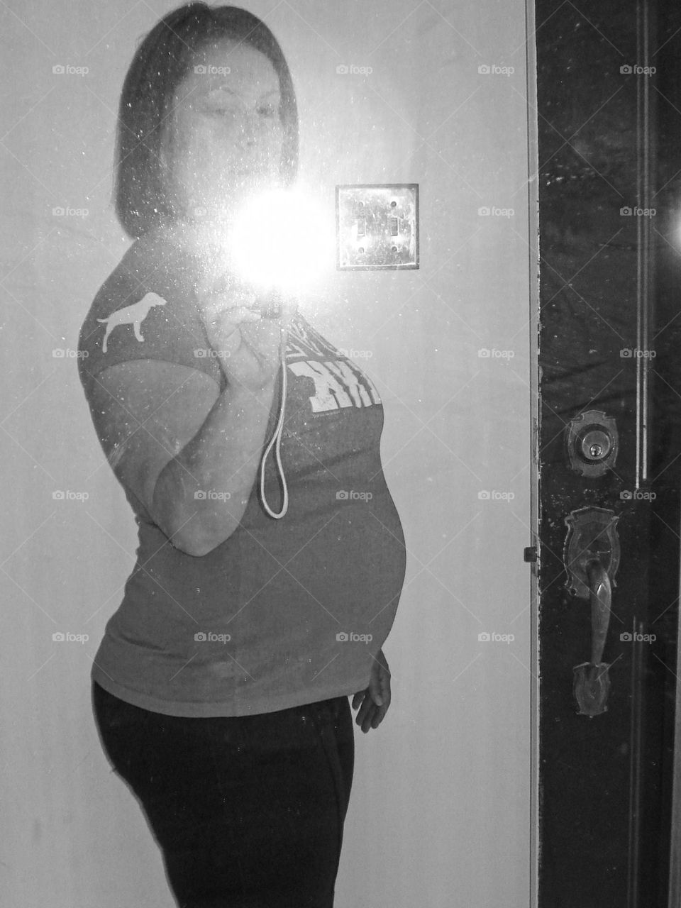 Selfie shot through a mirror of a pregnant lady in a front hallway.