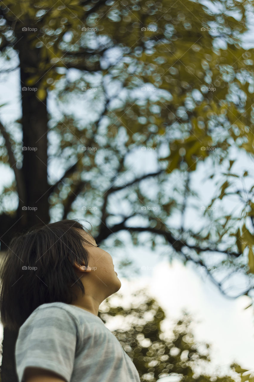 outdoor portrait of happy young eurasian boy on a blurry out of focus bokeh foliage background