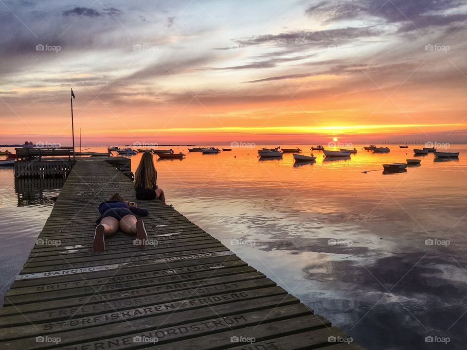 Woman photographing her friend sitting on pier