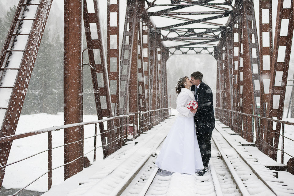 Newly married couple kissing on railway track during winter