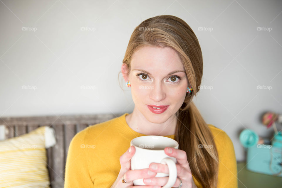 Portrait of a young woman holding a cup of coffee indoors and looking at the camera