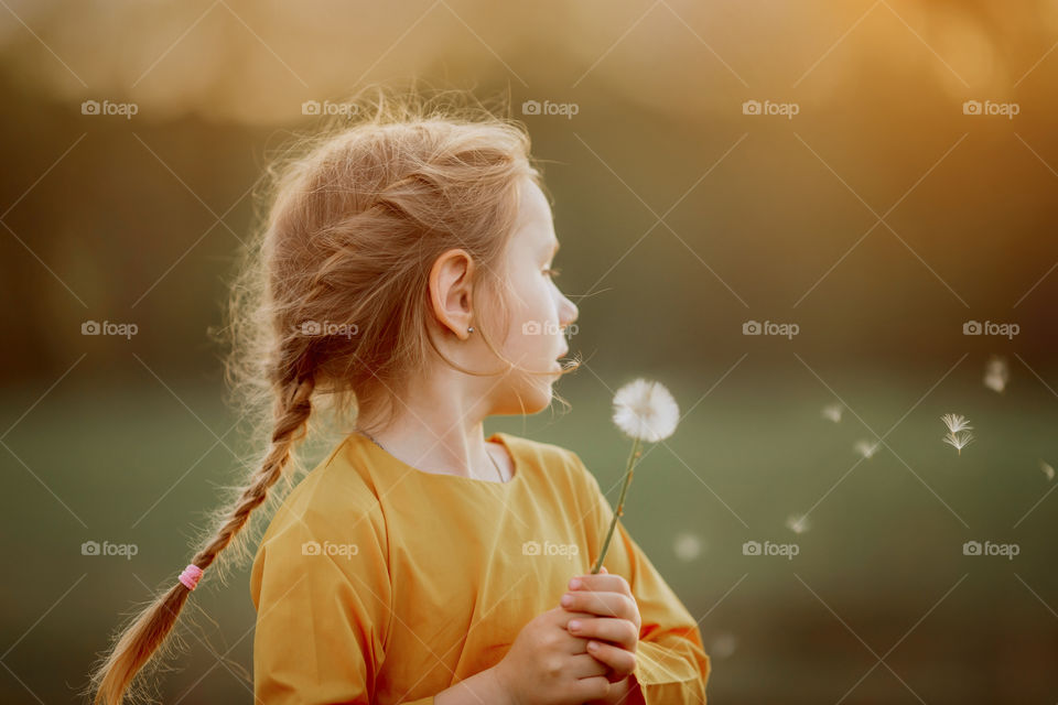 Little girl blowing dandelion at sunset