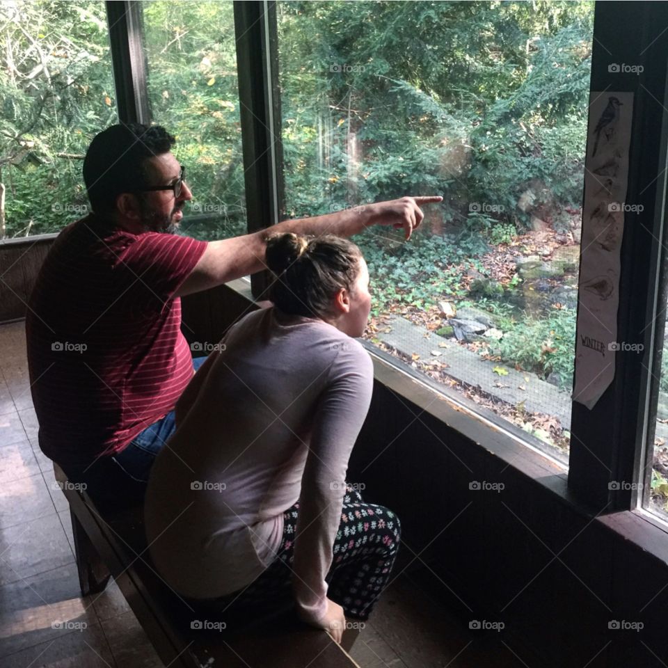 Father and daughter sitting inside viewing nature through a window 