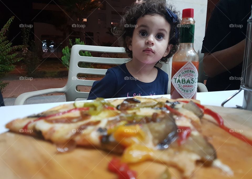 Slice of pizza in front of girl sitting on chair