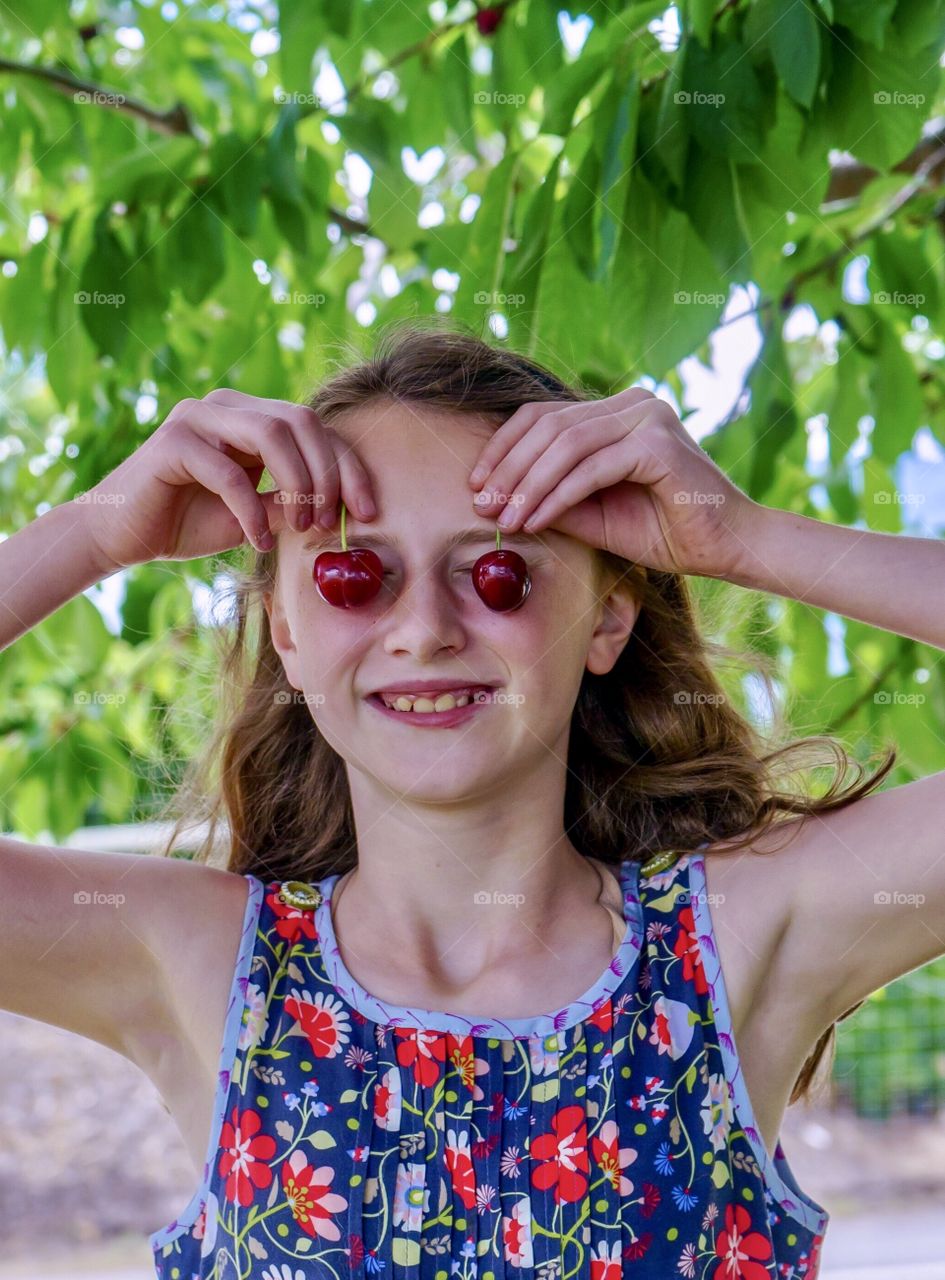 Girl holds cherries on eyes under cherry tree - fun portrait 