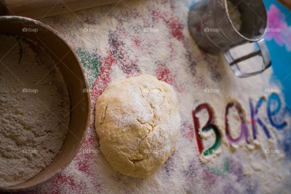 On the table lies a pastry for pies with sprinkled flour and a seeder for flour. Written to bake on the table.