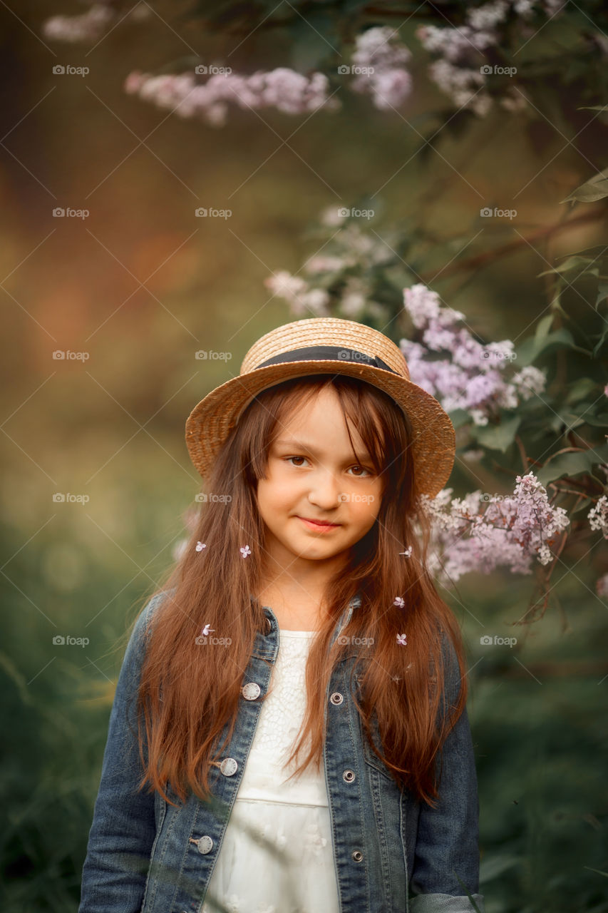 Little girl in a hat near blossom lilac tree at sunset 