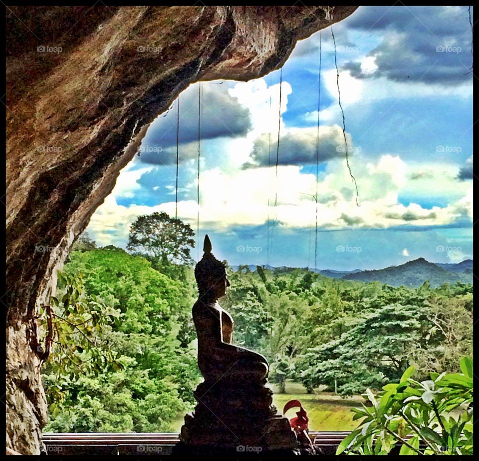 Buddha in a cave . This Buddha is tucked into a cave on a hillside overlooking mountains and a river in Thailand. 