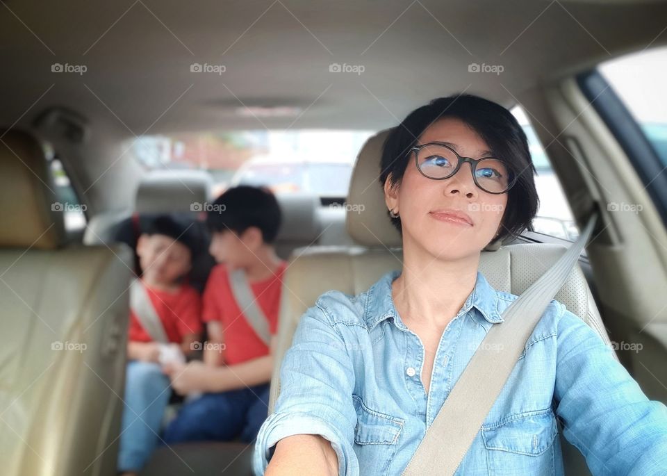Attractive asian mom driving a car in the city with her kids at the back seat. She concerning about driving safety by put on safety belt. - mom lifestyle