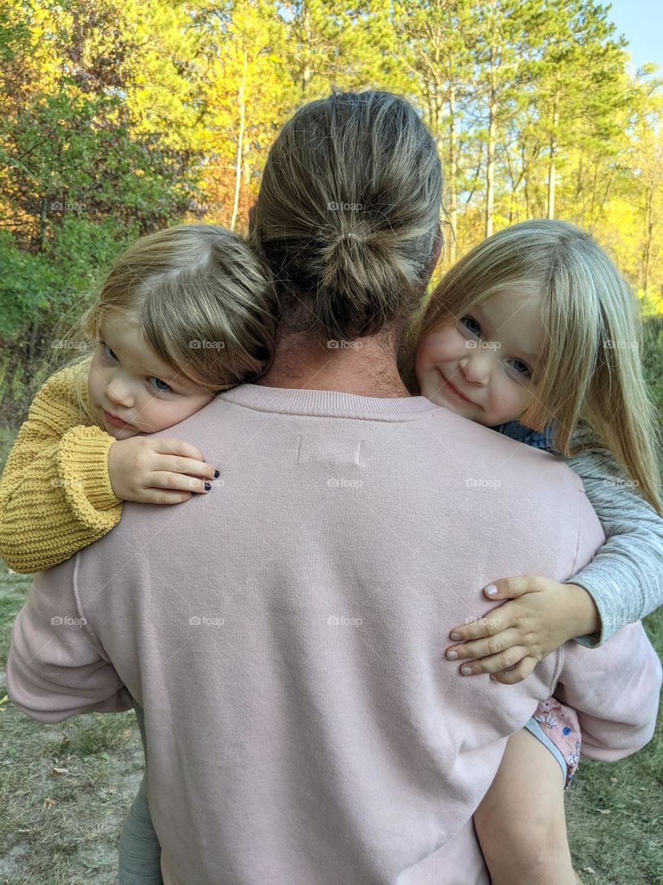 daddy holding two daughters laying on his shoulders, strong daddy, parent and kid bonding, small kid hands, dad bun, fall trees, fall colors, man bun, blonde kids, fall colors