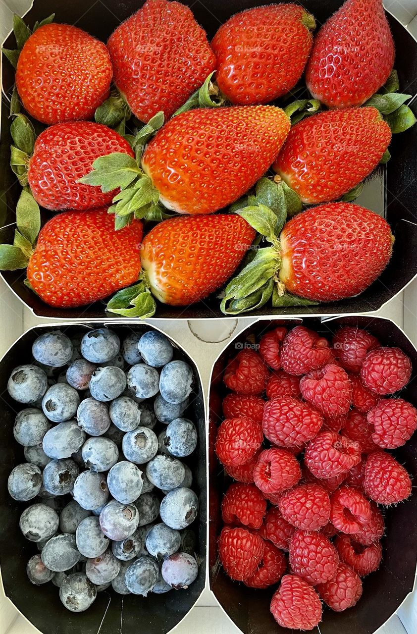 Assorted berries on paper boxes, strawberries, blueberries and raspberries seen from above 