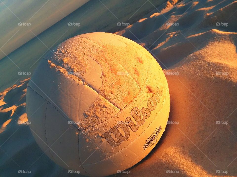 a Wilson volleyball laying in the sand, glowing with the light of a beautiful orange sunset