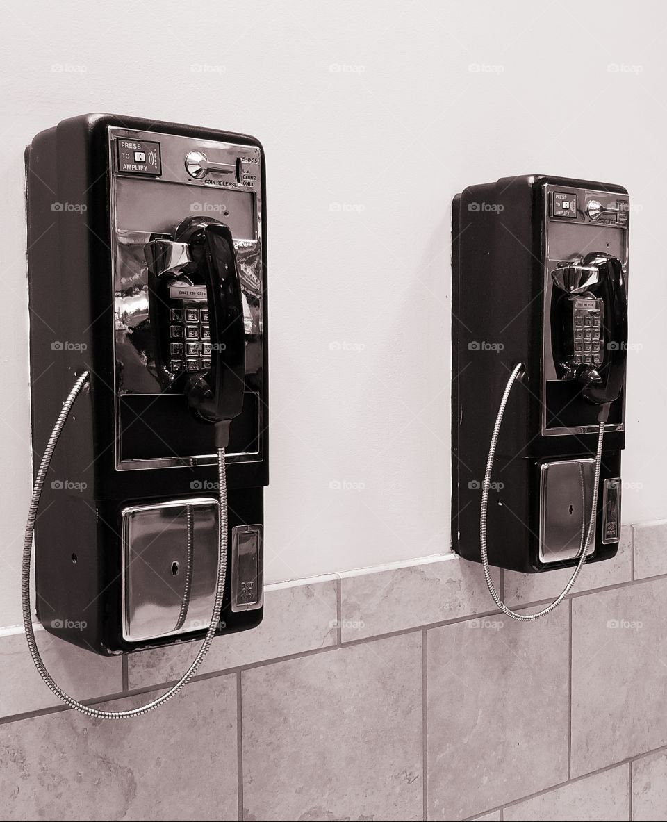Hey, Payphones! The photo is in black & white with a slight sepia tone.The chrome shines on the phone. The phones are in perfect cosmetic shape, & in perfect working order. There are two wall payphones units in the photo. They were for public use.