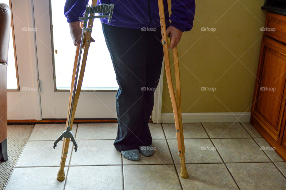 Woman using crutches with a reacher tool clipped on to them