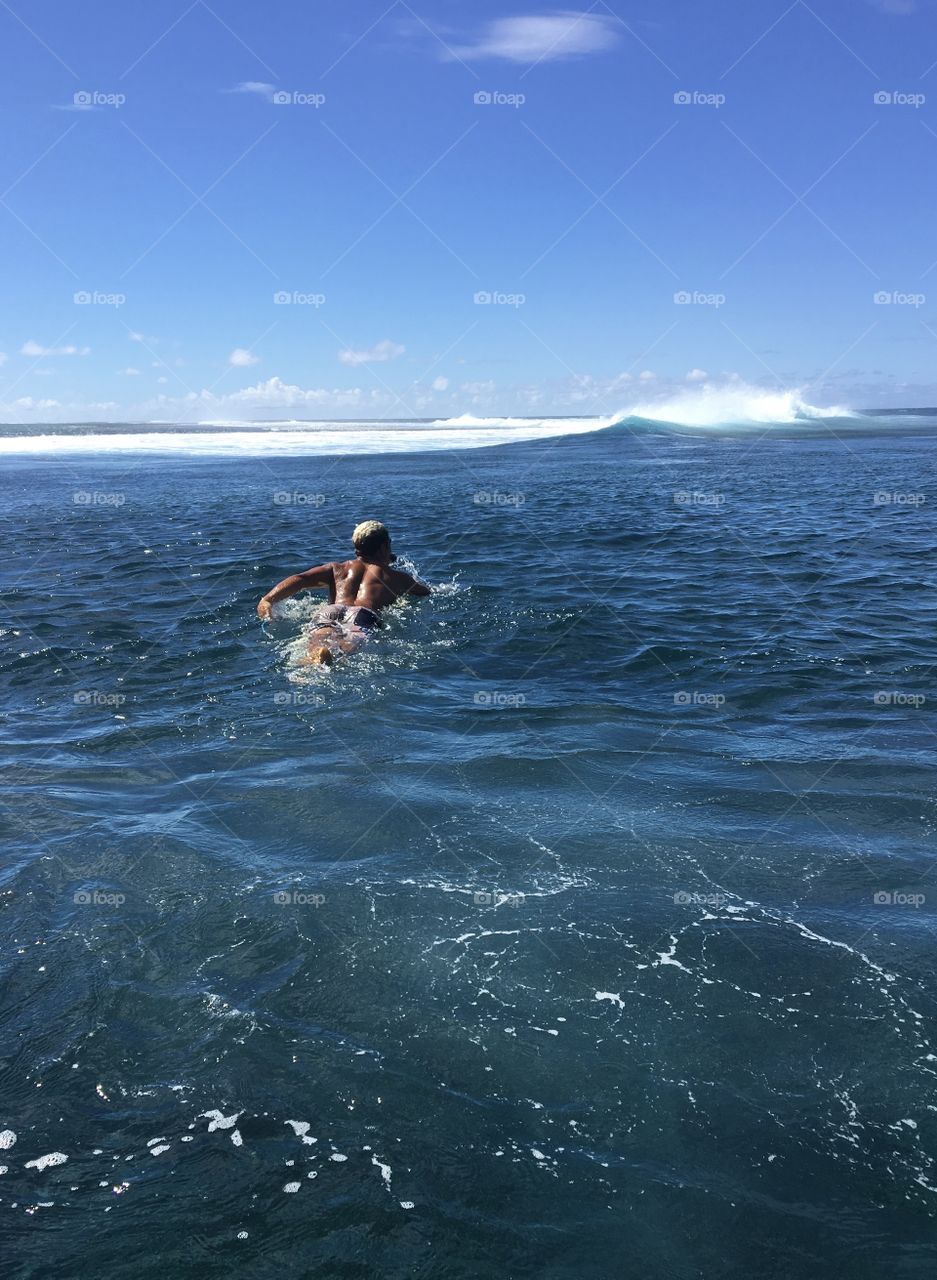 Young surfer swimming towards Teahupoo spot