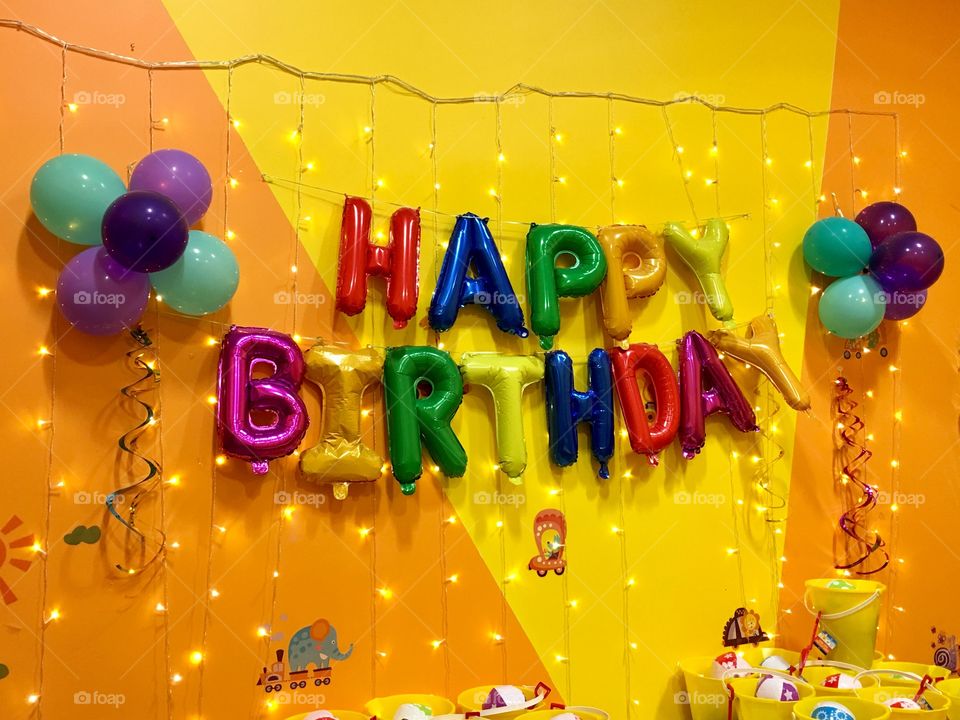 Happy Birthday spelled out with bold and colorful foil balloons on a yellow and orange wall